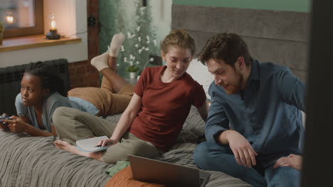 Caucasian-girl-and-boy-ar-talking-on-the-bed-in-bedroom-while-their-african-american-female-is-playing-video-games