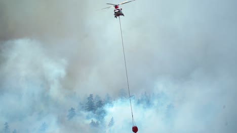 helicóptero con balde de agua, volando sobre humeantes bosques de incendios forestales, en el oeste de ee.uu.