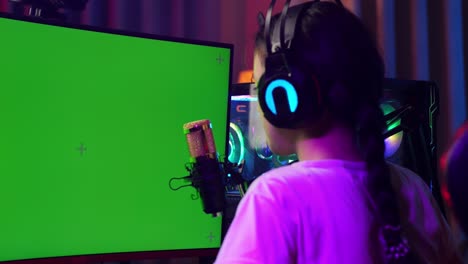 close up back view of asian girl streamer screaming goal celebrating winning game on green screen computer. live stream on desk illuminated by rgb led strip light