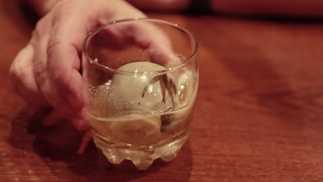 hand stirring a drink with an ice sphere