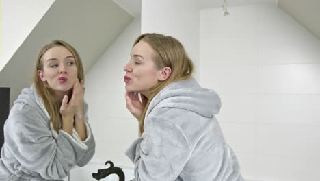 a young woman in a bathrobe next to a mirror watches her face