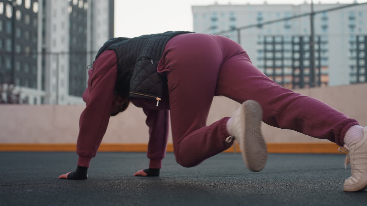 Back view of fitness instructor performing dynamic foot crawl exercise on urban sports court asphalt, hands pressed on floor while legs move rhythmically for core stability full body conditioning