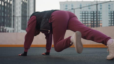 back view of fitness instructor performing dynamic foot crawl exercise on urban sports court asphalt, hands pressed on floor while legs move rhythmically for core stability full body conditioning