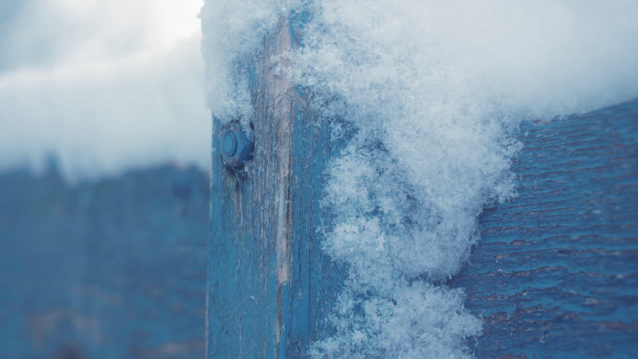 눈으로 인 오래된 나무 트레일러의 바르니치 볼트 근처에서 눈이 많이 내리는 동안 파란색 페인트가 어져 있습니다.