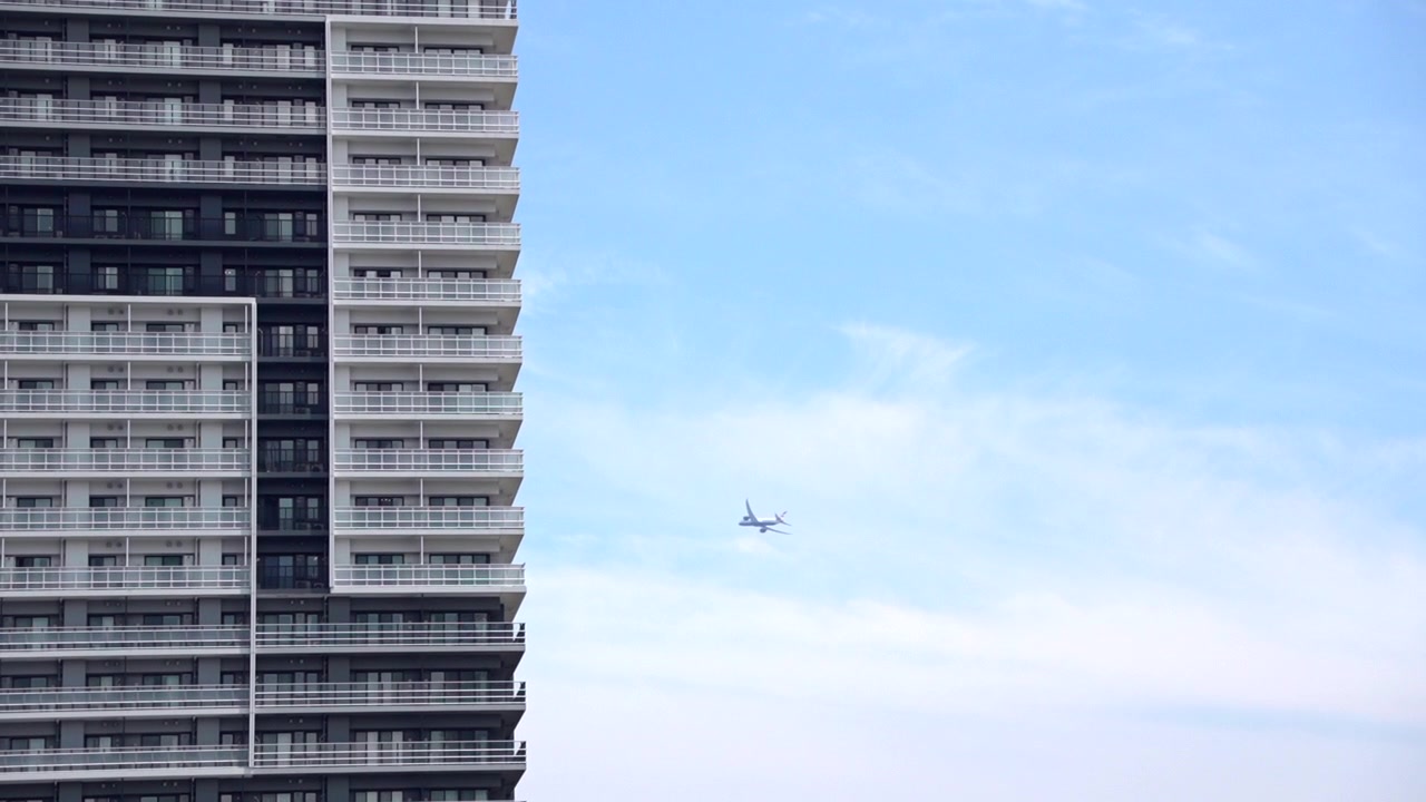 Un'inquadratura teleobiettivo incornicia un edificio da un lato e un cielo diurno limpido dall'altro. Un aereo scivola dietro l'edificio, creando una sorprendente giustapposizione.