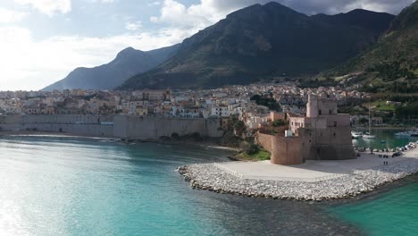 aerial flying over turquoise waters in the gulf of castellammare towards castello arabo normanno on sunny day