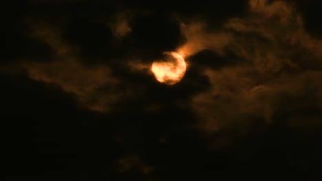 yellow moon or sun seen through patches of dark clouds moving in the wind