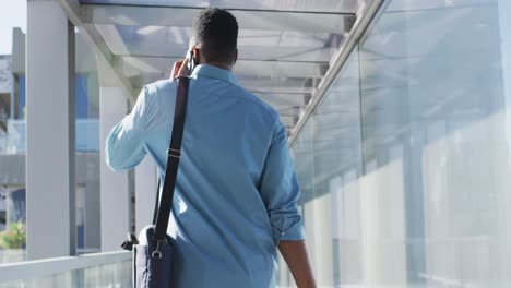 Video-of-back-view-of-african-american-man-walking-and-using-smartphone