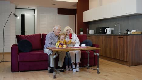 Senior-couple-grandparents-with-child-granddaughter-making-selfie-photos-together-on-mobile-phone