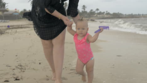 madre con la hija bebé caminando descalza por la playa