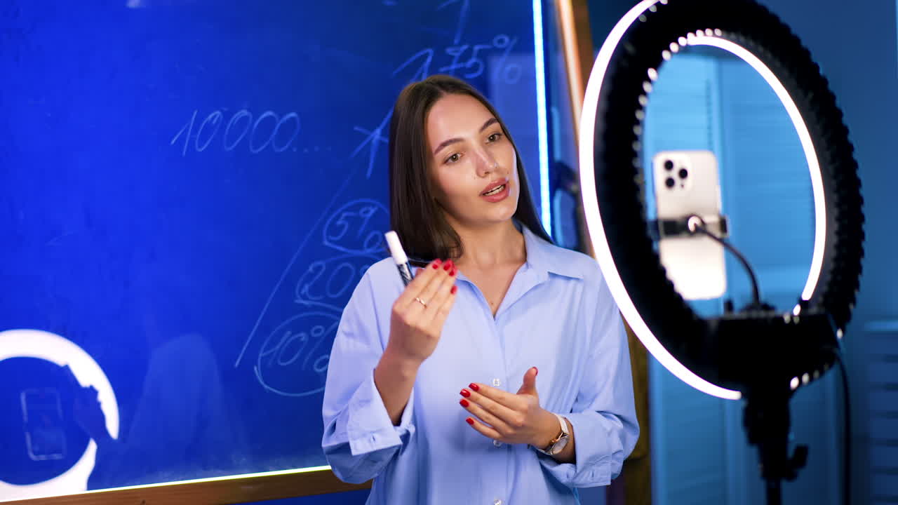 Educator talks finance online. A teacher presents finance concepts to students while using a whiteboard and ring light in a modern classroom setting