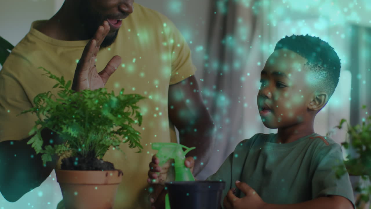 Animation of lights over happy african american father and son watering plants and clapping hands
