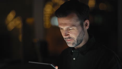 hombre caucásico adulto usando tableta digital en la oficina en la noche.