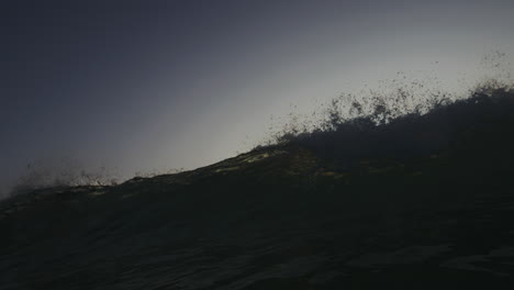 frontal view of wave breaking and crashing down spreading mist and green sunset light across water