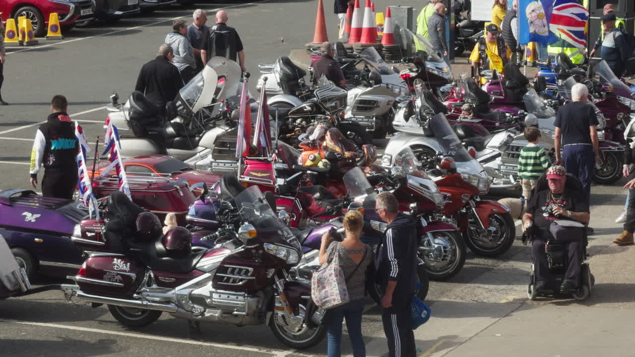 A group of motorcycle enthusiasts congregate at a seaside location, showcasing various Honda Goldwing models and engaging in lively discussions.
