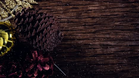 Animation-of-christmas-pine-cones-decoration-with-snow-falling-on-wood