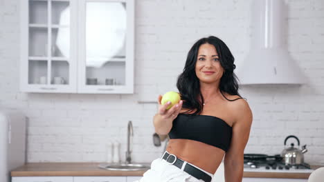 Gorgeous brunette woman sitting at the edge of the table and looking at the healthy apple. Diet and vegan food concept