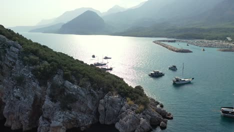 aerial view of scenic turkish coastline on mediterranean sea, harbor, anchored boat and islet at evening, drone shot