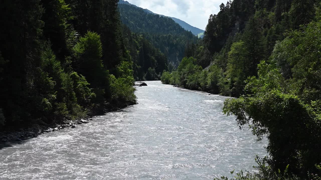 Grande fiume alpino con acqua glaciale che scorre nella valle, con una foresta di abeti accanto. Vallese, Svizzera.