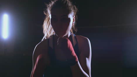 a beautiful female boxer strikes directly into the camera looking into the camera and moving forward on a dark background with a backlight. steadicam shot