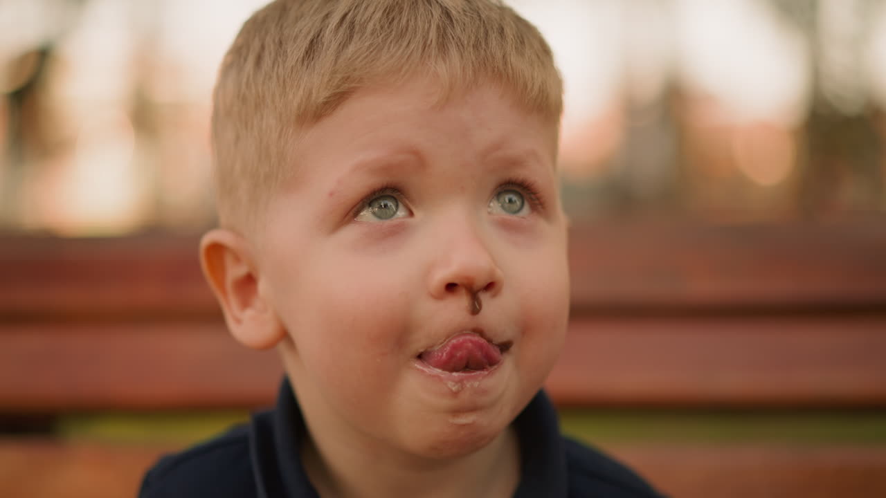 Divertente bambino lecca il cioccolato dalle labbra nel parco cittadino.