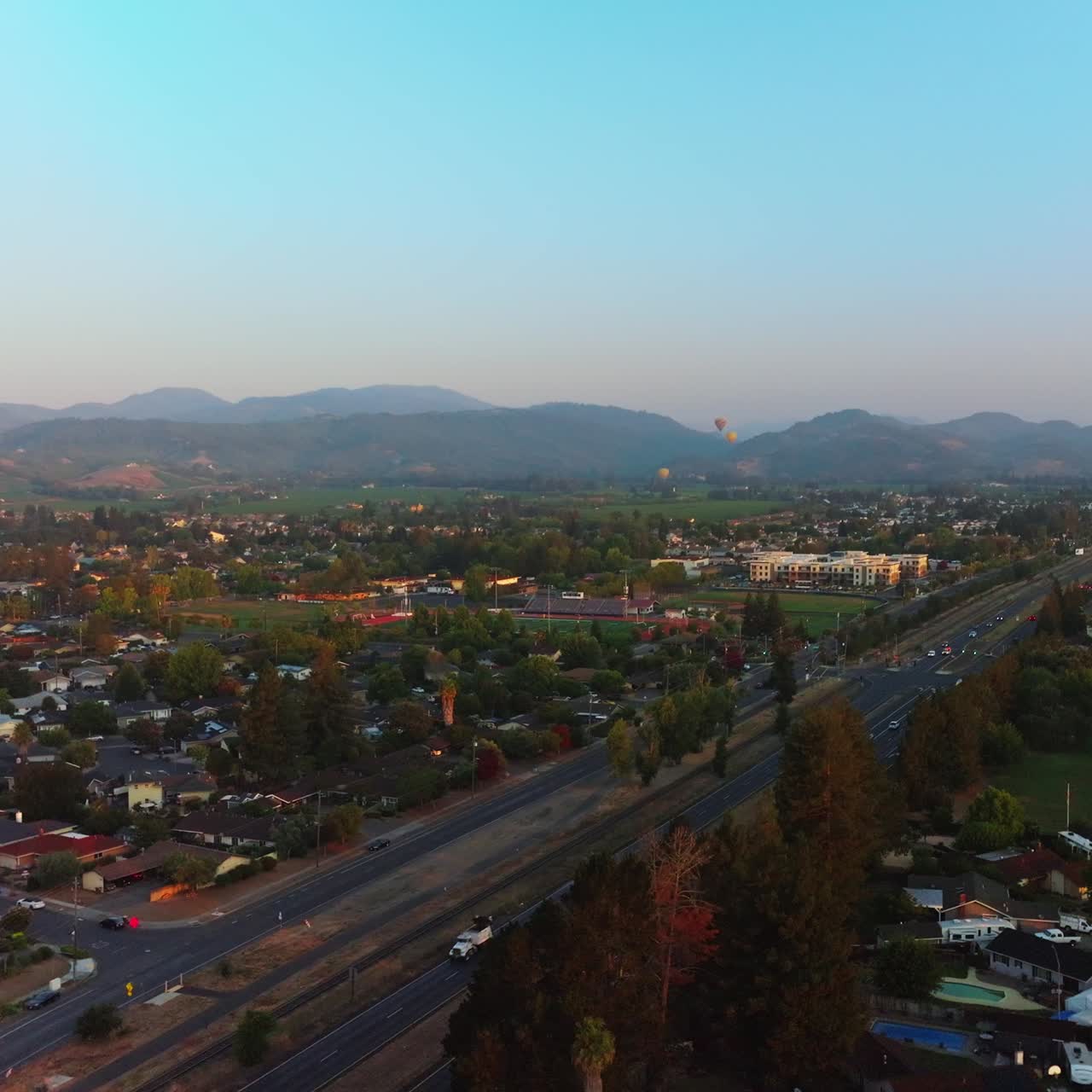 Roads full of cars in Napa, California, USA. Hot air balloons in the air over the city. Mountains at backdrop. Top view