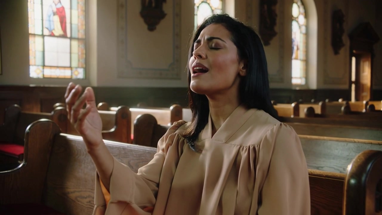 Sjungande kvinna i kördräkt med en psalm som börjar, höjer sedan sänker sin högra hand i kyrkan