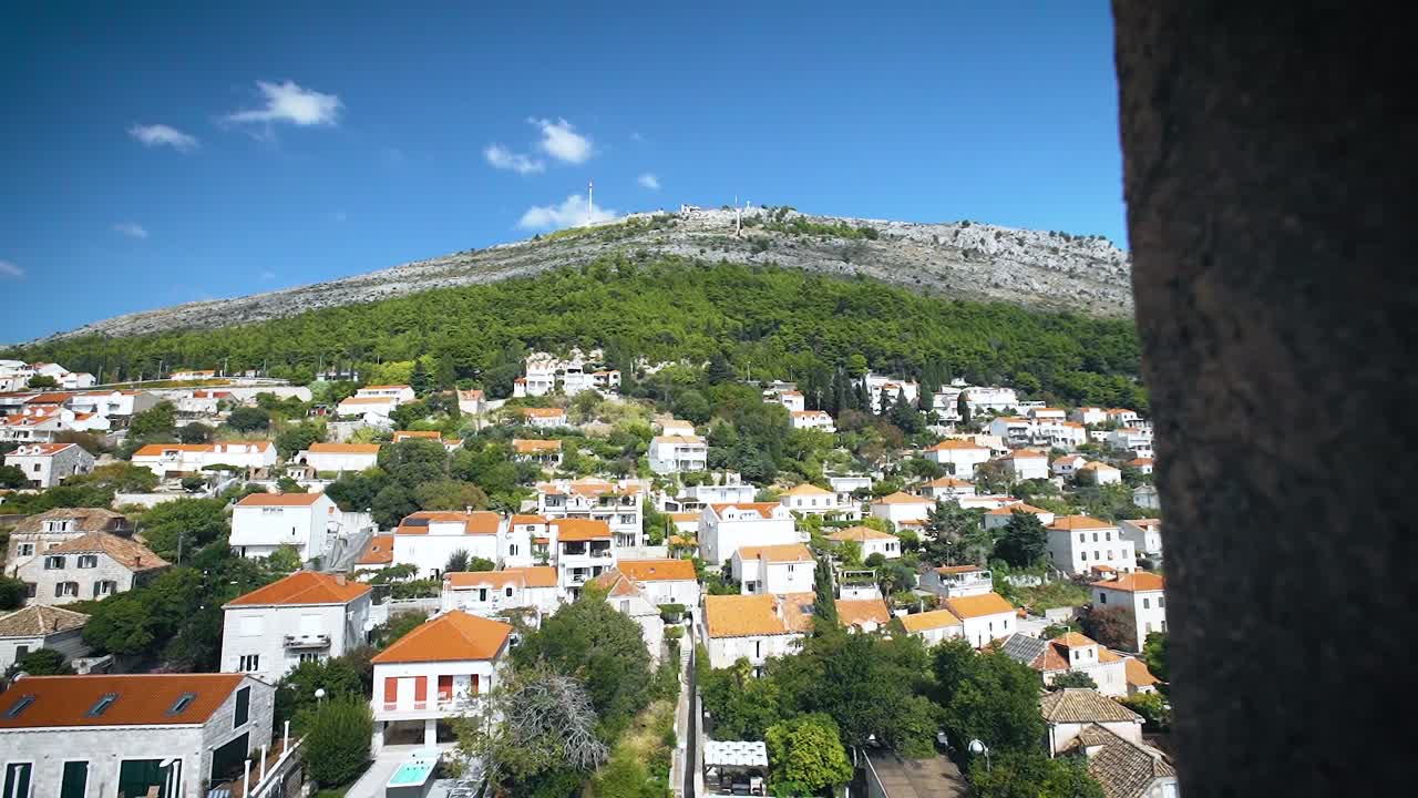 Peeking through a hole in the wall of Croatia’s walled city of Dubrovnik to reveal blue sky, hill and town in slow motion