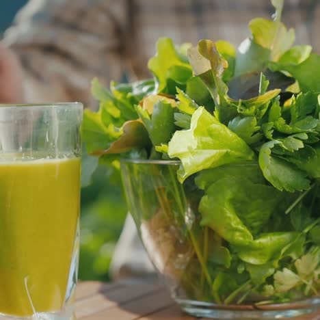 Eine-Frau-Stellt-Ein-Glas-Grünen-Smoothie-Neben-Einen-Teller-Mit-Salatblättern-Auf-Den-Tisch