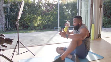 happy african american man resting making video call using smartphone at sunny home, slow motion