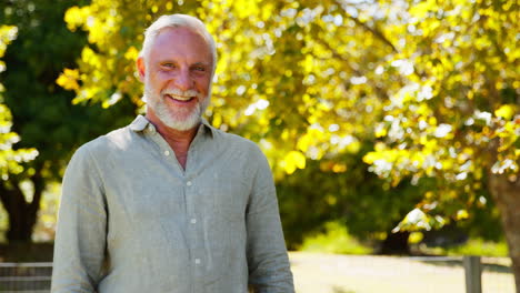 Retrato-De-Un-Hombre-Mayor-Sonriente-Parado-Al-Aire-Libre-En-El-Parque-Jardín-O-En-El-Campo