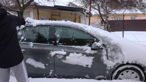 man brushing the snow off his car - medium shot