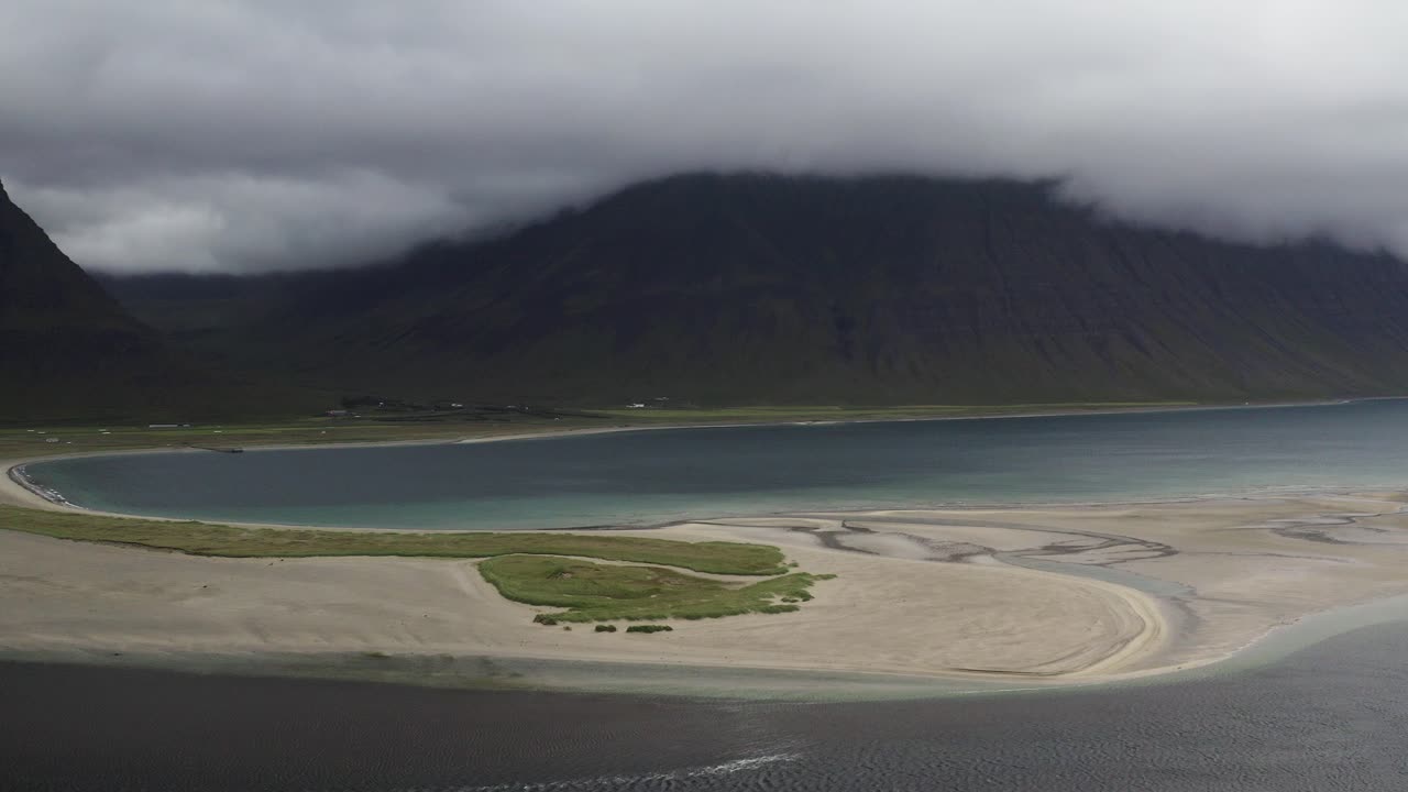 모래 섬 과 밀집 한 구름 으로  ⁇ 인 초록색 산 들 이 있는 오누다르피오르두르 피오르드 의 공중 사진