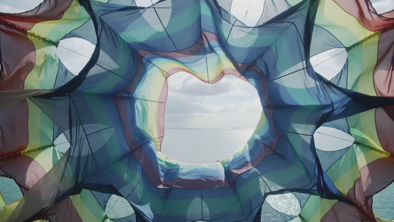 Billowing multicolor canopy in wind, showing widening star opening over sea sun glinting
