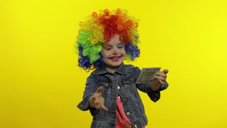 niña pequeña payaso en peluca colorida. dinero dólar billetes en efectivo ingresos cae desde arriba