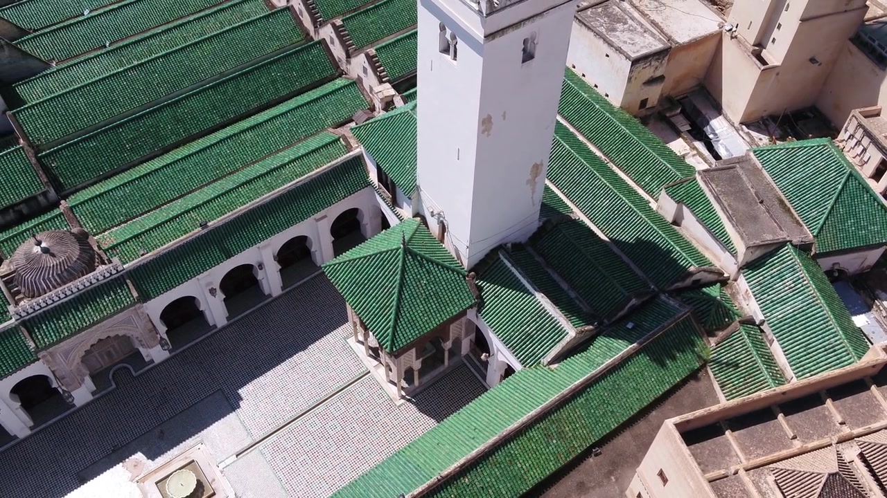Vista aerea elevata con drone dello storico minareto bianco, degli archi del cortile e dei tetti in tegole smaltate verdi della Moschea Al Quaraouiyine a Fez, Marocco.