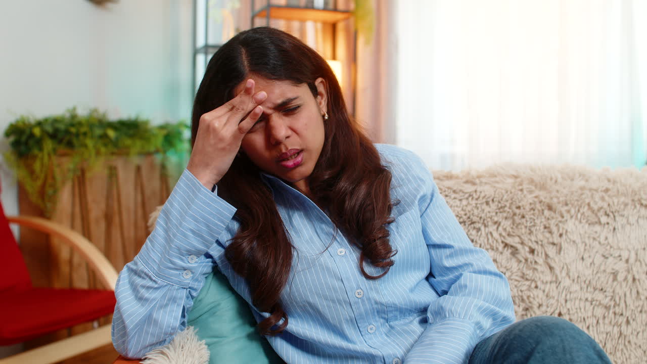 Indian woman touching head with tension and pain from headache at home exhausted and uncomfortable