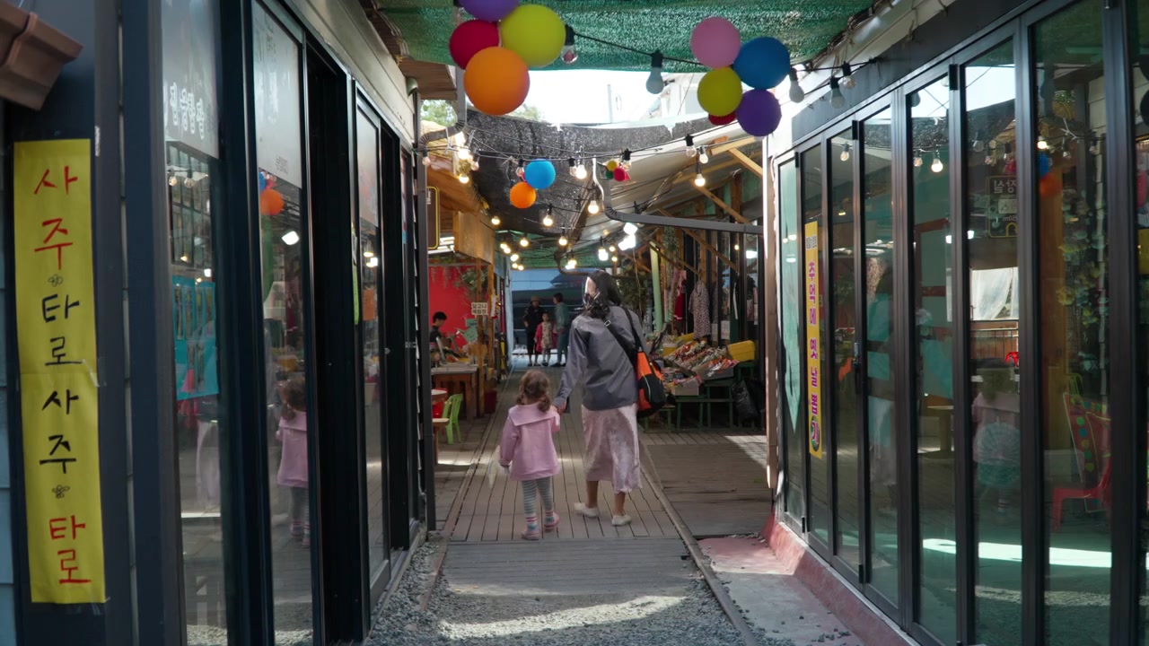 Back view of Little Girl With Mom Walking on Railroad Tracks in Gyeongamdong Railroad Town Exploring Old Retro Shops