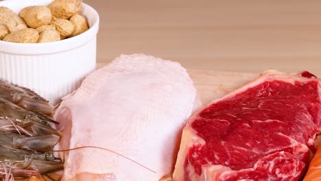 a selection of raw meats and nuts displayed on a wooden board for culinary presentation.