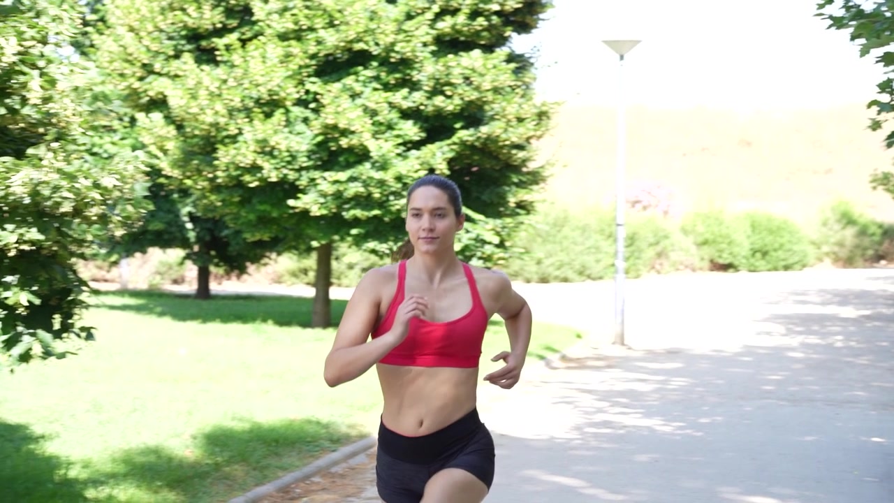I en sommerpark løber en ung atletisk kvinde udendørs og fremmer sundhed og fitness.