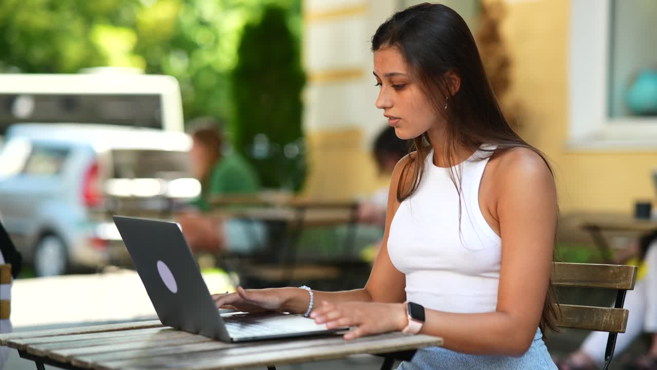 mujer joven trabajando en una computadora portátil en un café al aire libre