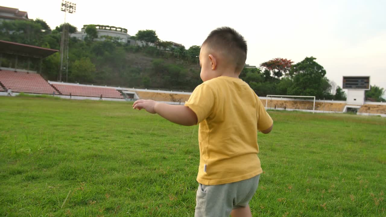 Asian Little Boy Running On The Grass At Stadium