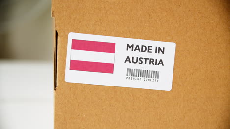 manos aplicando la etiqueta de la bandera de austria hecha en una caja de cartón de envío con productos