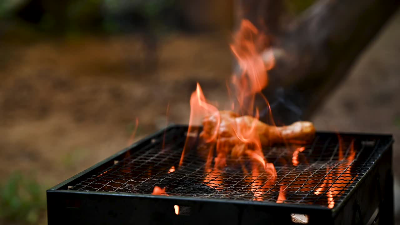 Dramatic slow-motion shot of a chicken leg being grilled over open flames on a barbecue. The sizzling fire, smoky heat, and juicy meat create a mouthwatering cooking scene perfect for food visuals