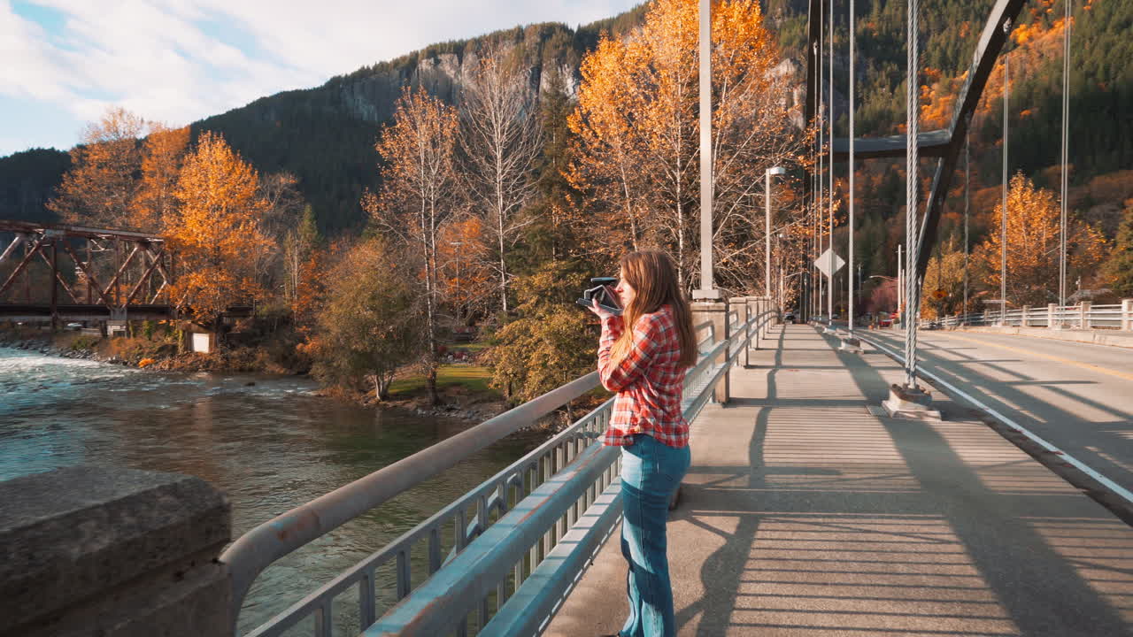 la mujer fotógrafa toma una foto polaroid del valle desde el puente entre los colores del otoño