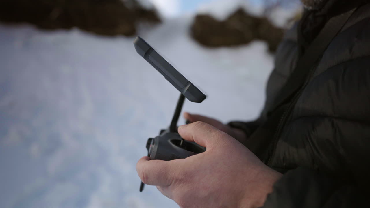 Male hands operating a drone controller outdoors on a snowy landscape with cold winter clothing