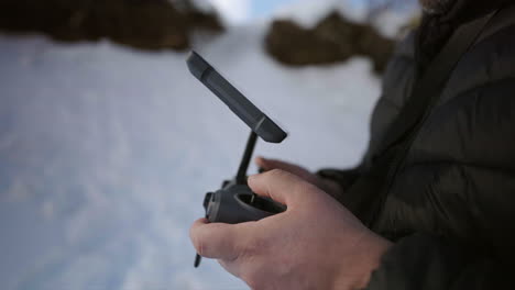 male hands operating a drone controller outdoors on a snowy landscape with cold winter clothing