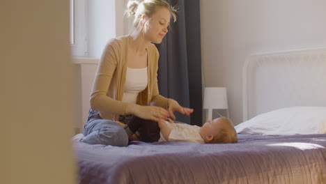 madre feliz abrazando y jugando con su bebé en la cama en casa