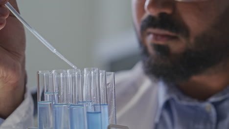 chemist using pipette to dispense blue liquid into multiple test tubes