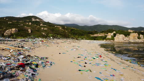 Aerial-view-ocean-pollution-in-Asia,-drone-reveal-piles-of-plastic-waste-and-garbage-trash-on-a-sandy-tropical-beach-in-Vietnam